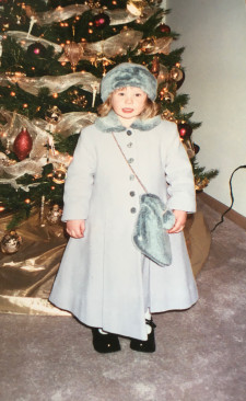 A photo of Samantha Morehead dressed up in a blue jacket and matching winter hat in front of a Christmas tree.