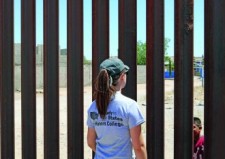 A student speaks with a child on the other side of the border fence.