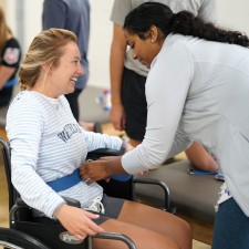 A student practices strapping another student into a wheelchair.