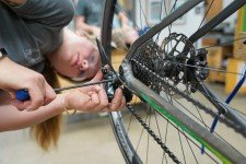Smucker using a screwdriver on a bike wheel's chain assembly.