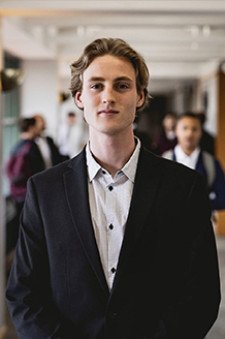 Photo of Eric Isaksson wearing a dark suit in the hallway of Schneider Hall