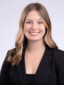 Madison Dober, wearing a black shirt and black blazer, smiles at the camera for her professional headshot. 