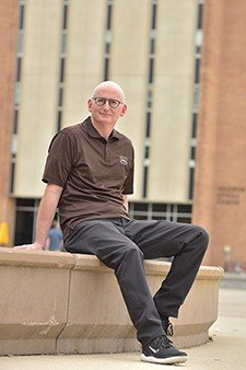 Photo of Michael Braun sitting on the edge of Campus Fountain outside Sprau Tower.