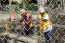 Two construction workers in hardhats behind a fence.
