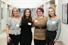 Team members for The Lux Scrub, Rachel Millett, Julia Haas, Mandy Sorensen and Paige Roden, stand together in a hallway in Schneider Hall. 