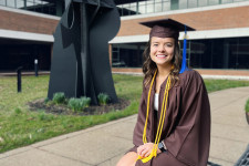 Kallie Mac seated outside in her WMU cap and gown for graduation.