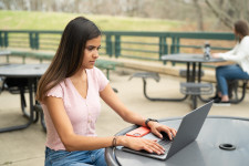 A students works on a laptop at a table outside.