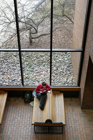 photo of a student on a bench next to a wall of windows, shot from above