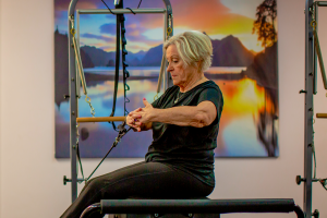 Lady sitting on a pilates machine pulling back machine straps