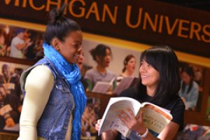 Two WMU students smiling at each other. One student is holding an opened book.