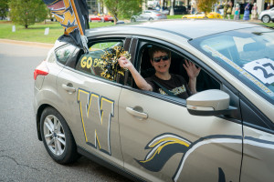 A passenger waves out the window of a car decorated in WMU spirit.