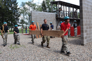 An ROTC cadet helps campers carry a large plank of wood to complete a scenario on the leadership reaction course.