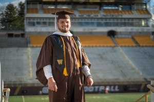 Mike Caliendo stands on the football field in his cap and gown.