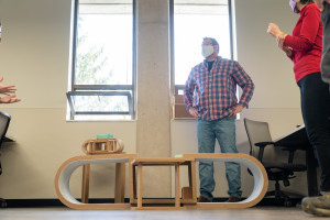 A student stands behind a table and chairs he designed.