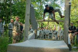 An ROTC cadet jumps over a wooden hurdle.