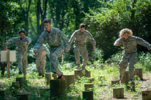 Teenagers in Army fatigues leap between stumps on an obstacle course.