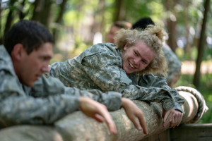 A teenager in Army fatigues smiles at another squad member.