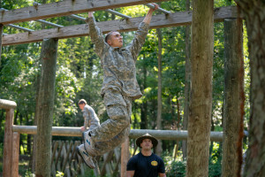 A teenager in Army fatigues crosses monkey bars.