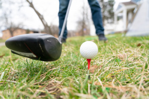 A golf club next to a teed up ball.
