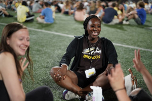A student sits on the field at Waldo Stadium with a group of other students.