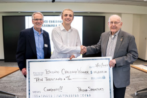 Three people hold a large check and shake hands.