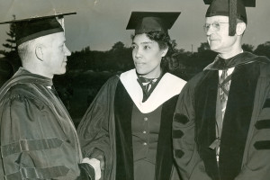 A black and white photo of three people in graduation regalia.