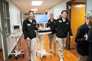 Three WMU students push a cart through the a hospital hallway.