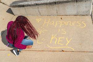 A student writing "Happiness is key" in chalk.