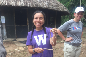 Female student in WMU shirt smiles while holding a snake in Belize.