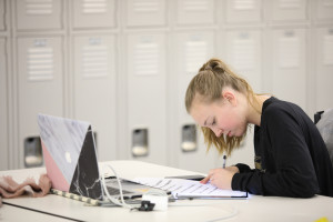 a student writing at a desk with a laptop open.