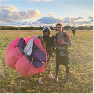 Two men stand in a field with a parachute.
