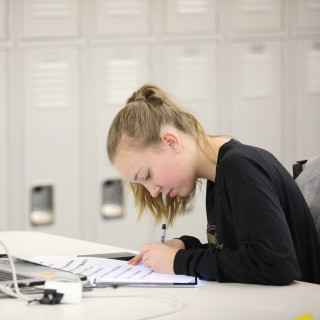 student at a desk in front of laptop, writing.