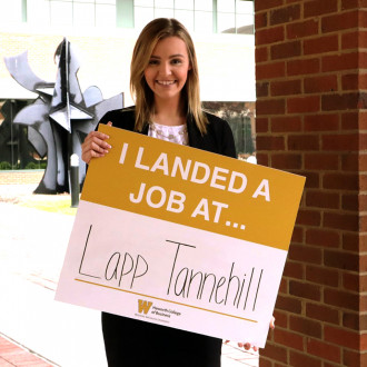 Pictured is a student holding a sign that says I got a job at Lapp Tannehill