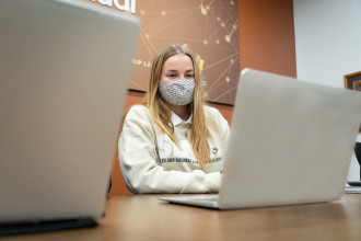 Masked student sitting at laptop inside sales lab