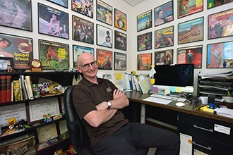 Michael Braun sitting in his office chair surrounded by album covers hanging on the wall