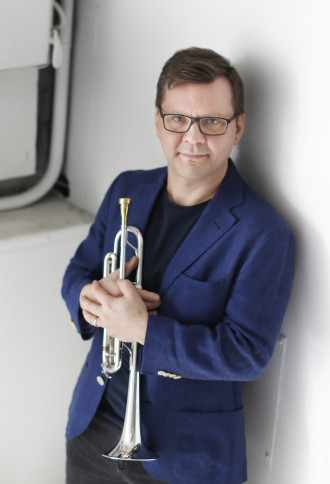 Pasi Pirinen holding trumpet to his chest, leaning against a wall.