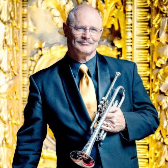 Terry Everson with trumpet in front of ornate background.