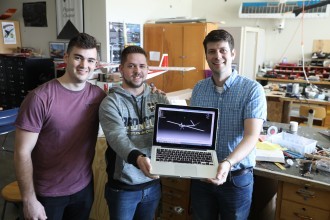 Three male WMU students holding a laptop in their laboratory.