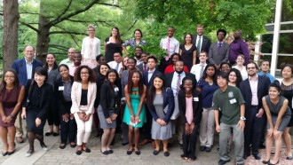 A diverse group of students and faculty in formal summer clothes smiling at the camera.