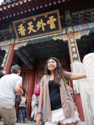 A female WMU student standing in front of a door with Chinese writing, laughing.