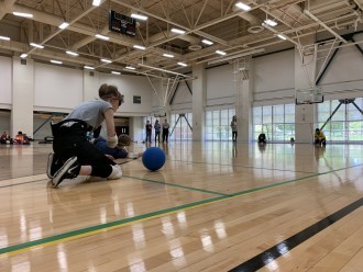 A female athlete in an indoor field crouches to play goalball.