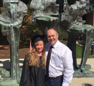 A young woman in a graduation cap and gown poses with her professor.