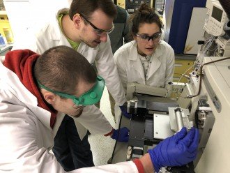 Students in lab coats analyze samples with a mass spectrometer.