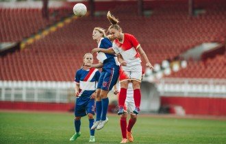 A female soccer player uses her head to take the ball from an opponent.