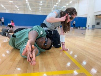 A counselor sprawls out on the floor to teach an athlete how to dive after a ball.