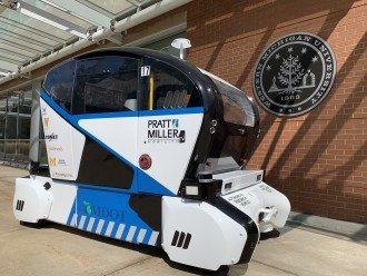 Photo of a blue and white autonomous vehicle next to a brick wall featuring Western Michigan University's seal.