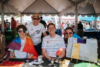 Four people sit at a rainbow-colored table for Kalamazoo Pride.