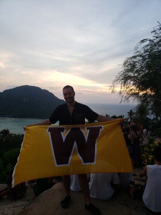 Dylan Coleman holds a large gold flag with a brown "W" on it in a tropical setting.