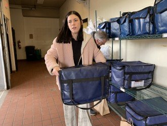 A young woman carries a cooler filled with food out of a storage room.