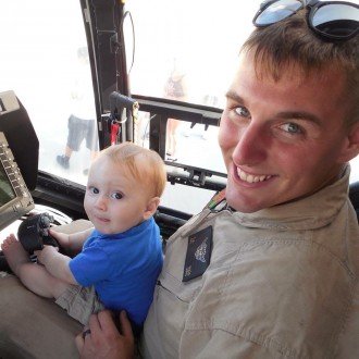 Troy Duck sits in the cockpit of a military plane with his baby son on his lap.